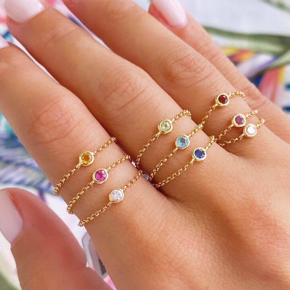 18K gold chain rings featuring colorful birthstones displayed on a hand, showcasing elegance and personal significance.