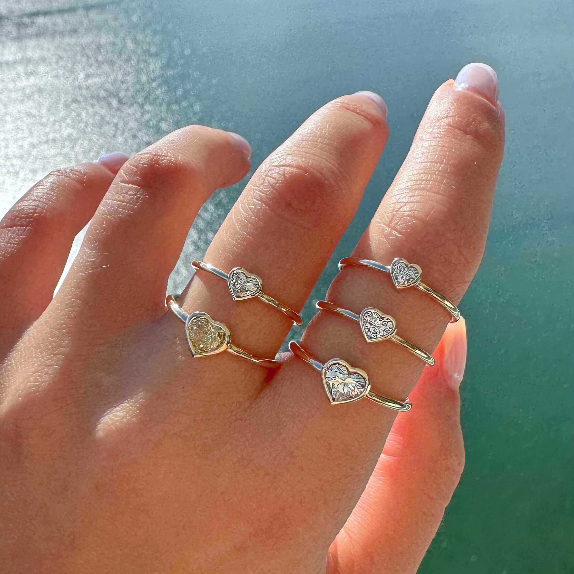 Hand wearing multiple gold rings with heart-shaped diamond designs from our jewelry collection.