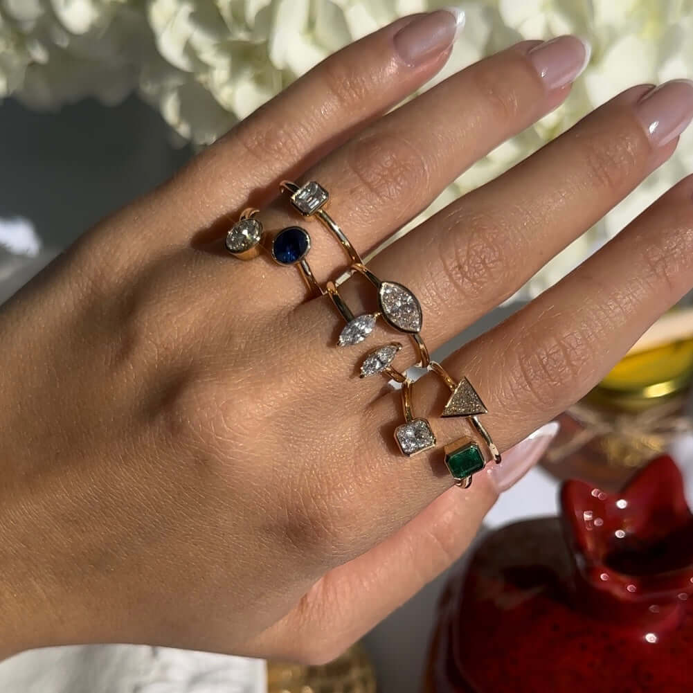 Elegant hand wearing multiple unique gold rings with diamonds and colored gemstones, showcasing modern jewelry design.