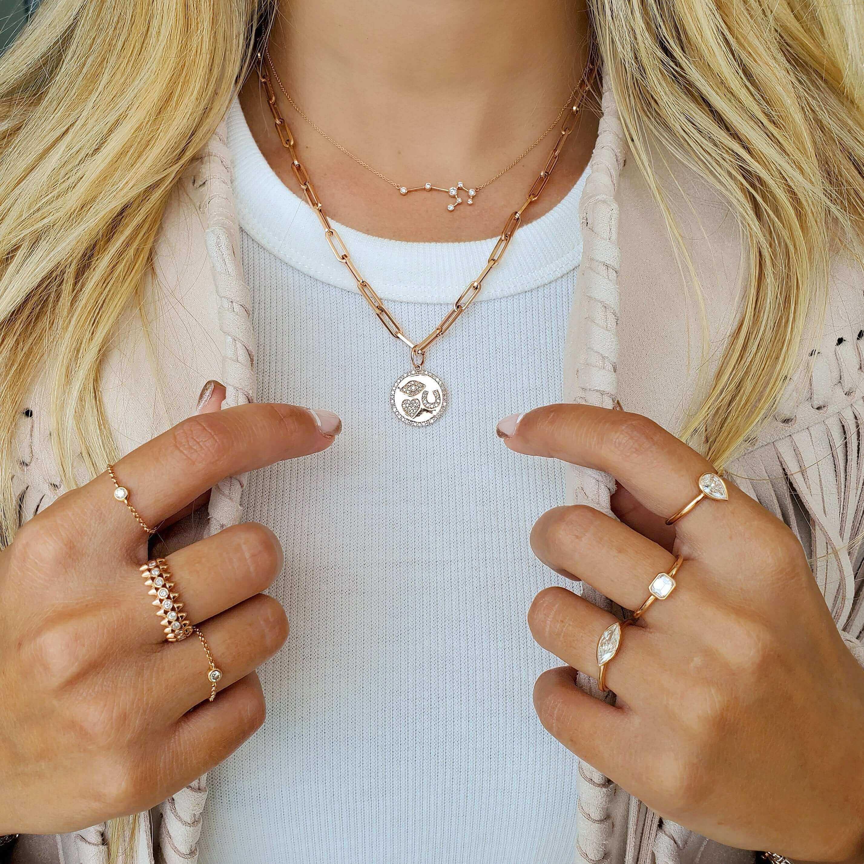 Close-up of a woman wearing layered necklaces and multiple rings, showcasing fine jewelry and celestial designs.