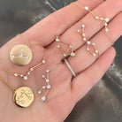 18K gold zodiac constellation diamond necklaces displayed on a hand, showcasing elegant designs and sparkling diamonds.