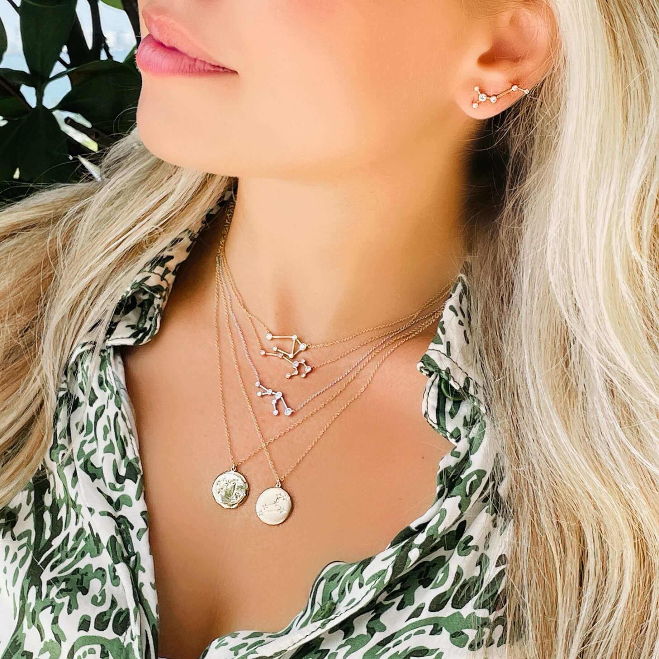 Woman wearing layered 18K gold zodiac constellation diamond necklaces, showcasing celestial designs and elegant style.