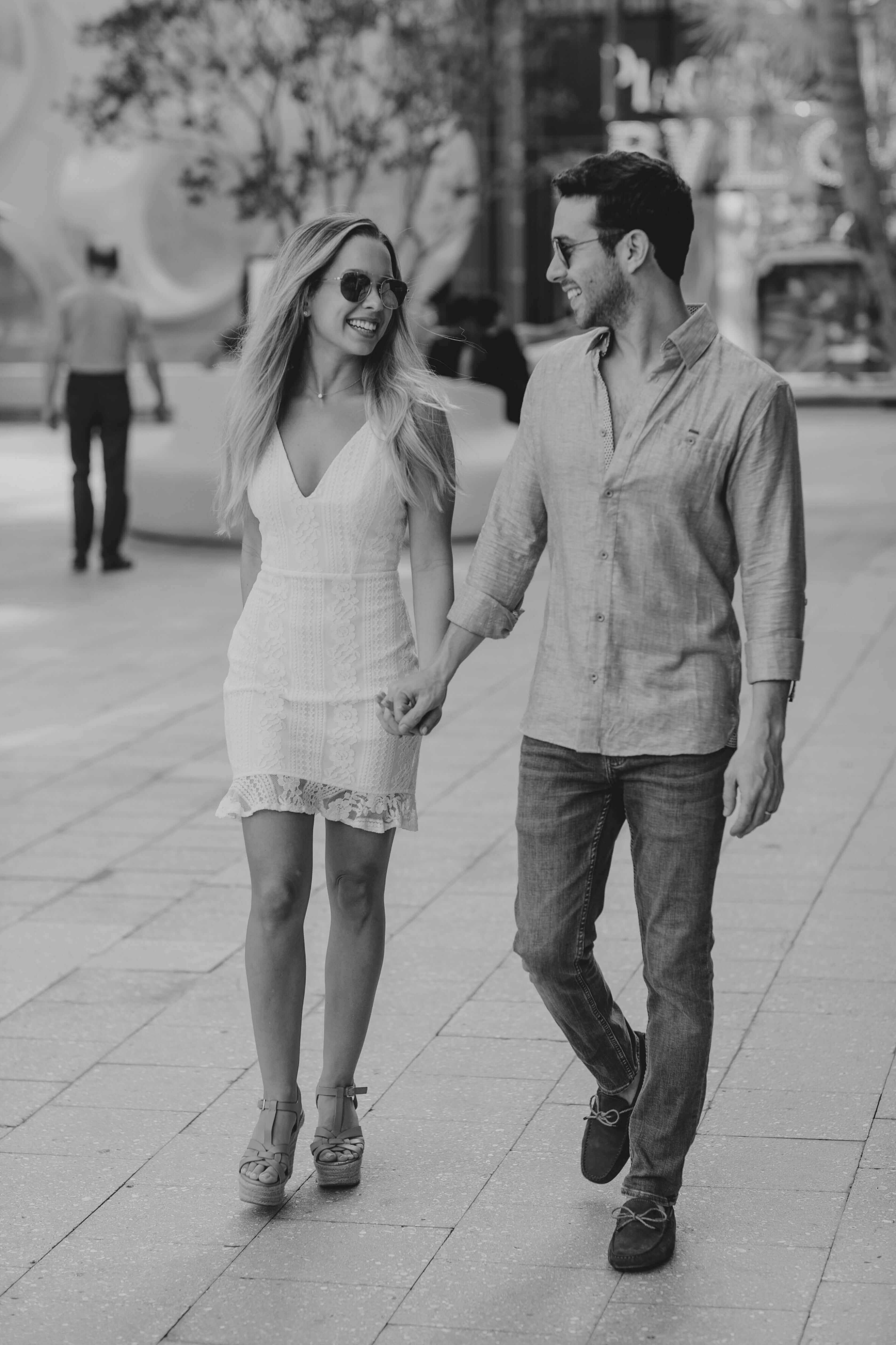 Couple walking hand in hand on a city street, enjoying a sunny day together, showcasing love and connection.