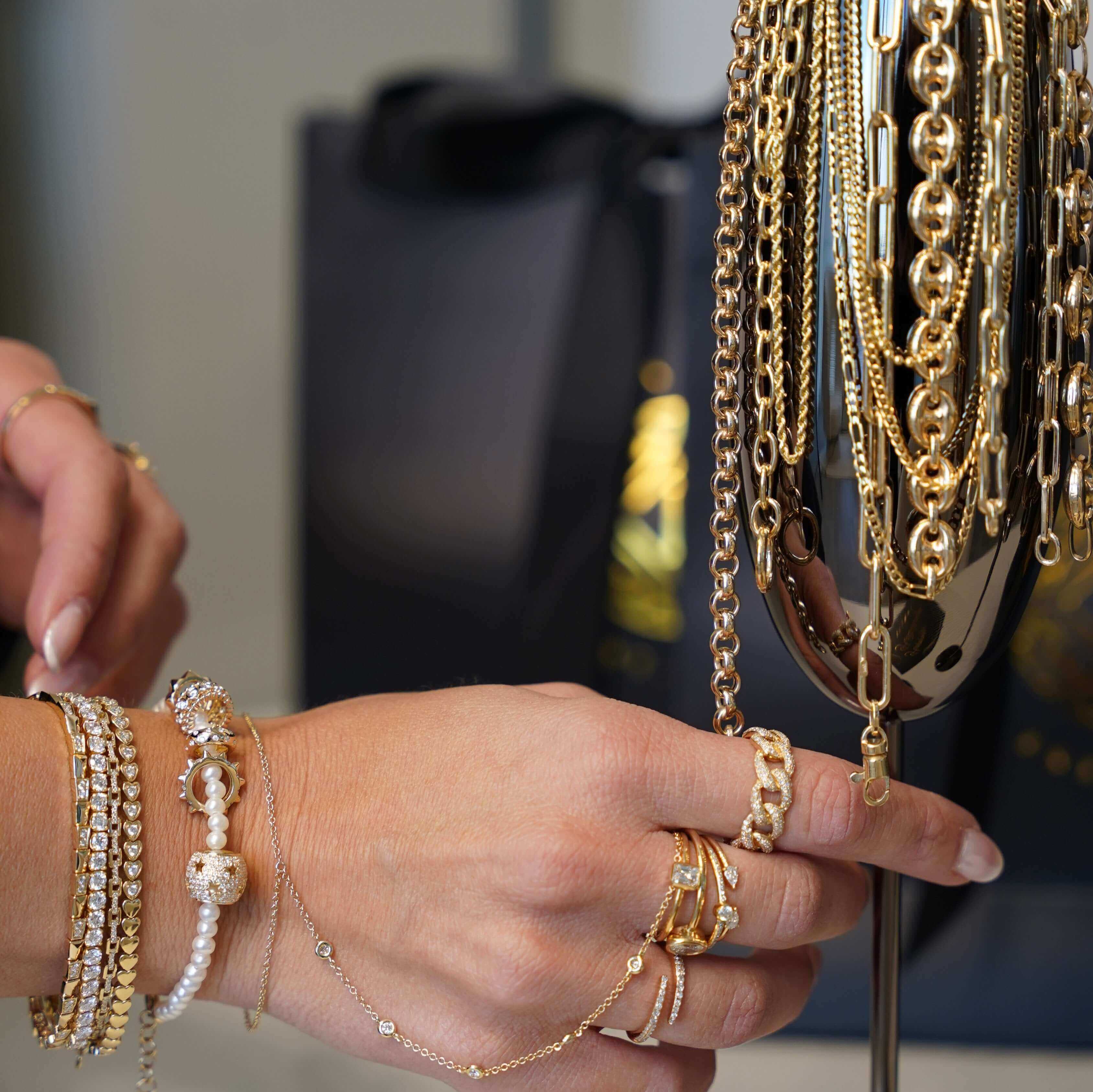 Close-up of hands showcasing elegant gold and silver jewelry, including bracelets and necklaces, with a luxury shopping bag in the background.