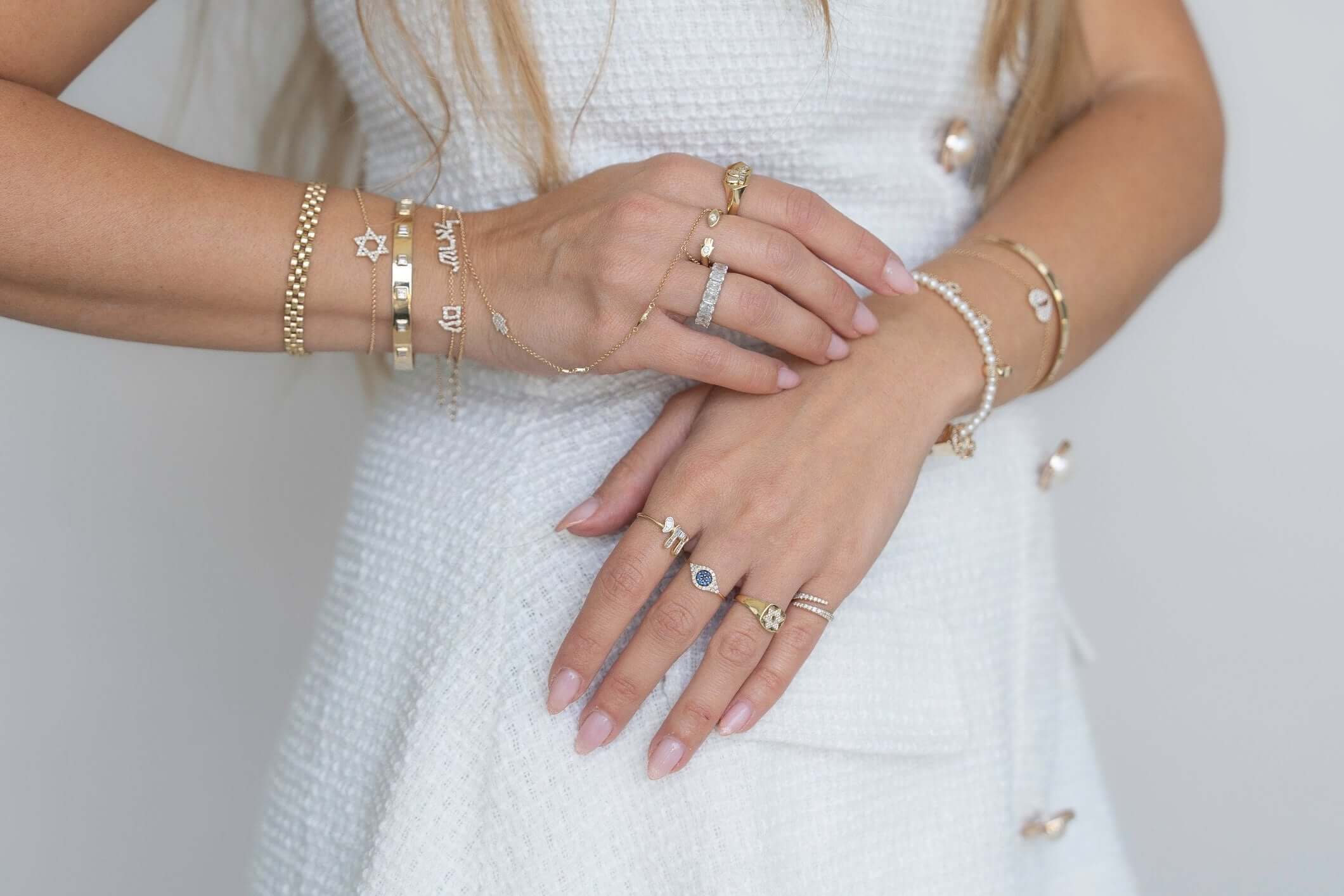 Close-up of hands adorned with various gold bracelets and rings, showcasing unique jewelry styles.