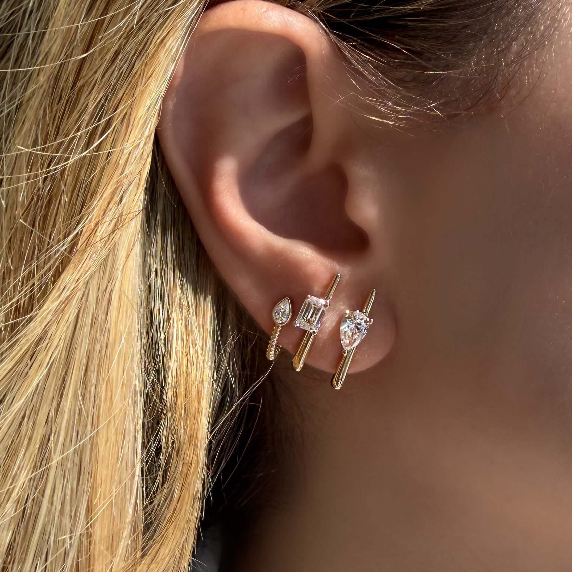 Lab Diamond Bar Stud Earrings showcased on ear with pear shaped and emerald cut diamonds in sleek gold bars.