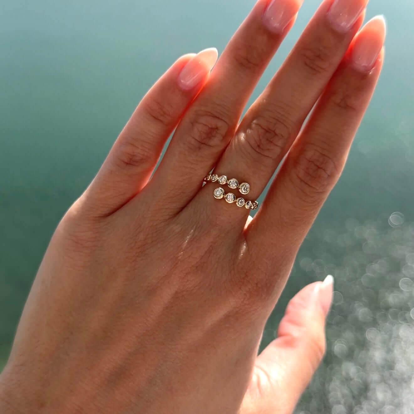 Diamond Bezels Wrap Ring on a hand with smooth gold bezels and brilliant round diamonds against a sunny backdrop.