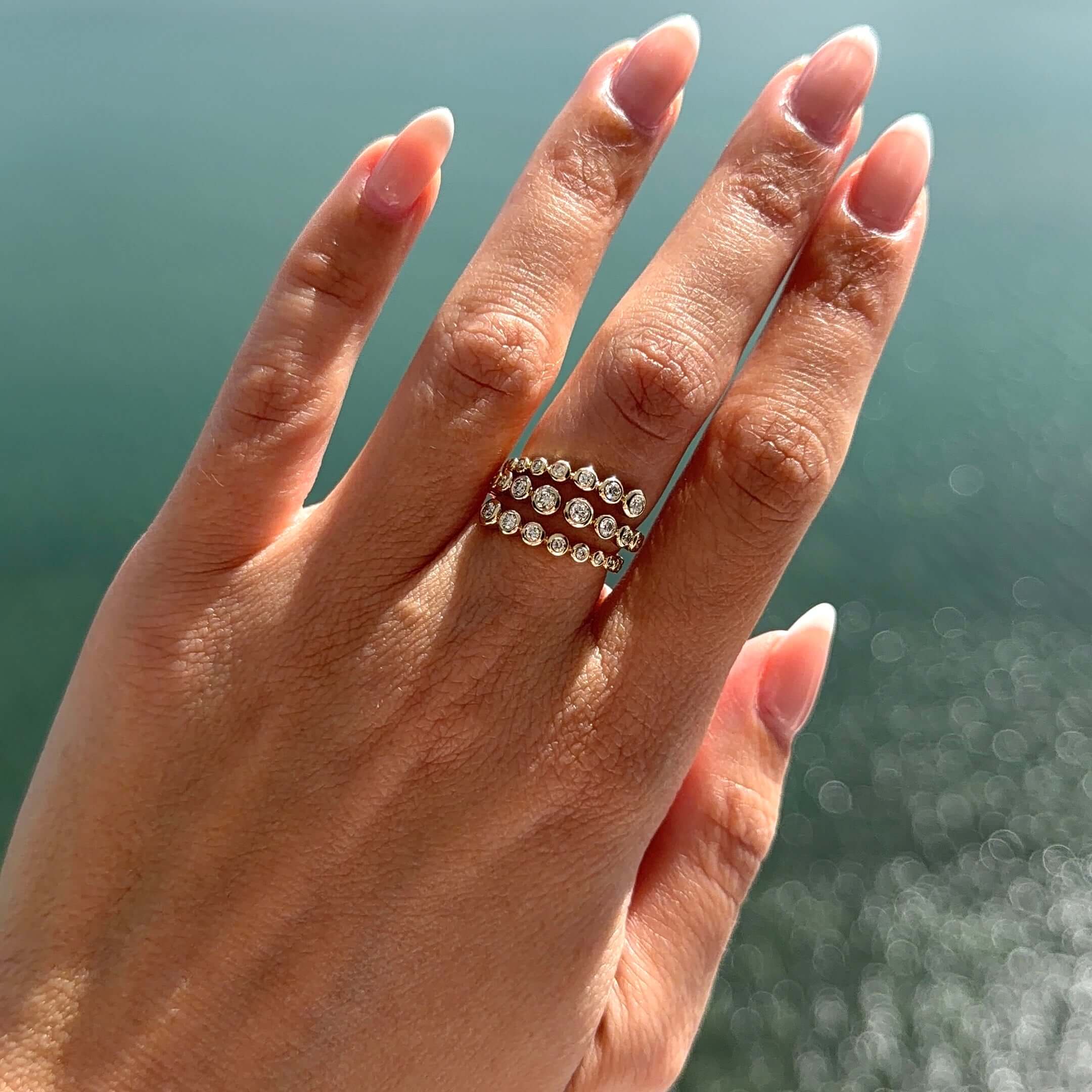 Diamond Bezels Wrap Ring worn on hand, showcasing brilliant round diamonds in gold bezels against shimmering water.