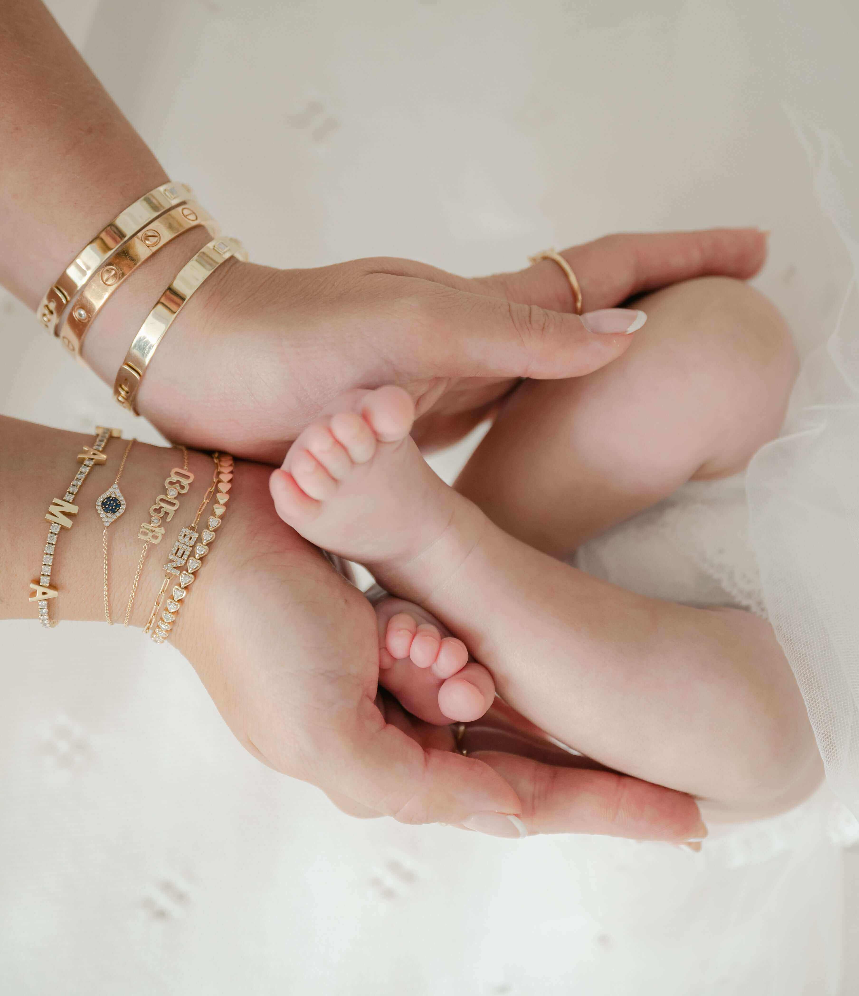 Hands holding a baby's feet, showcasing Izakov Fine Jewelry bracelets, symbolizing love and tenderness.