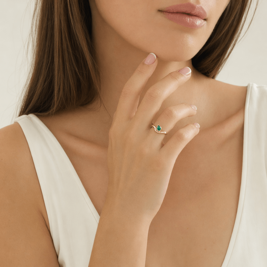 Pear Shaped Emerald Curved Ring worn on a woman's finger, showcasing its unique design and vibrant emerald in yellow gold.
