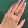 Curved Lab Diamond Bezel Ring worn on a hand with soft pink nails against a water background.