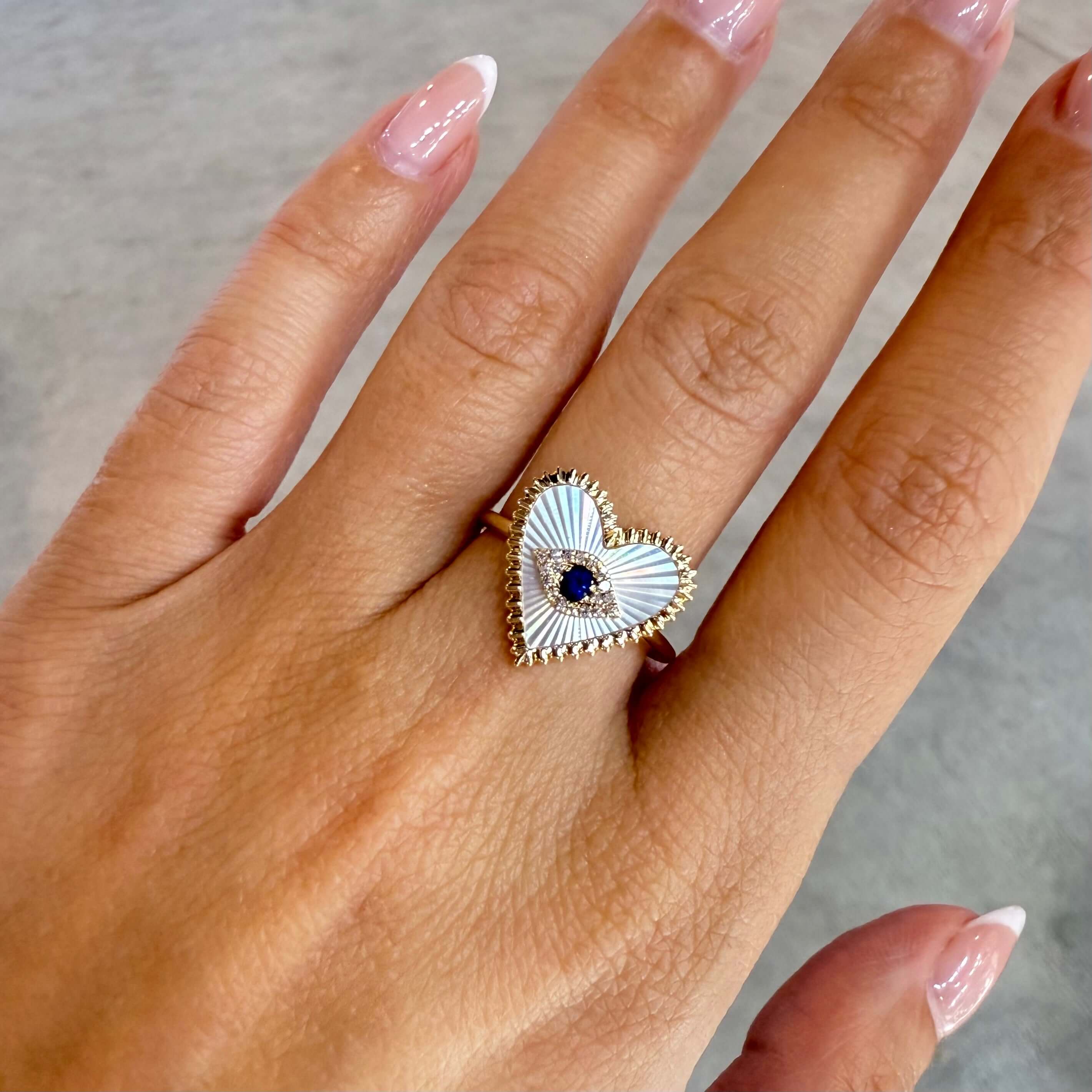 Radiating Gemstone Heart Evil Eye Diamond Ring worn on a finger with elegant manicure, showcasing its unique design and details.