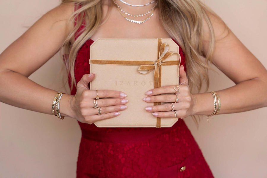 Woman in red dress holding an Izakov Fine Jewelry gift box, showcasing beautiful 14k gold jewelry from Miami, Florida.